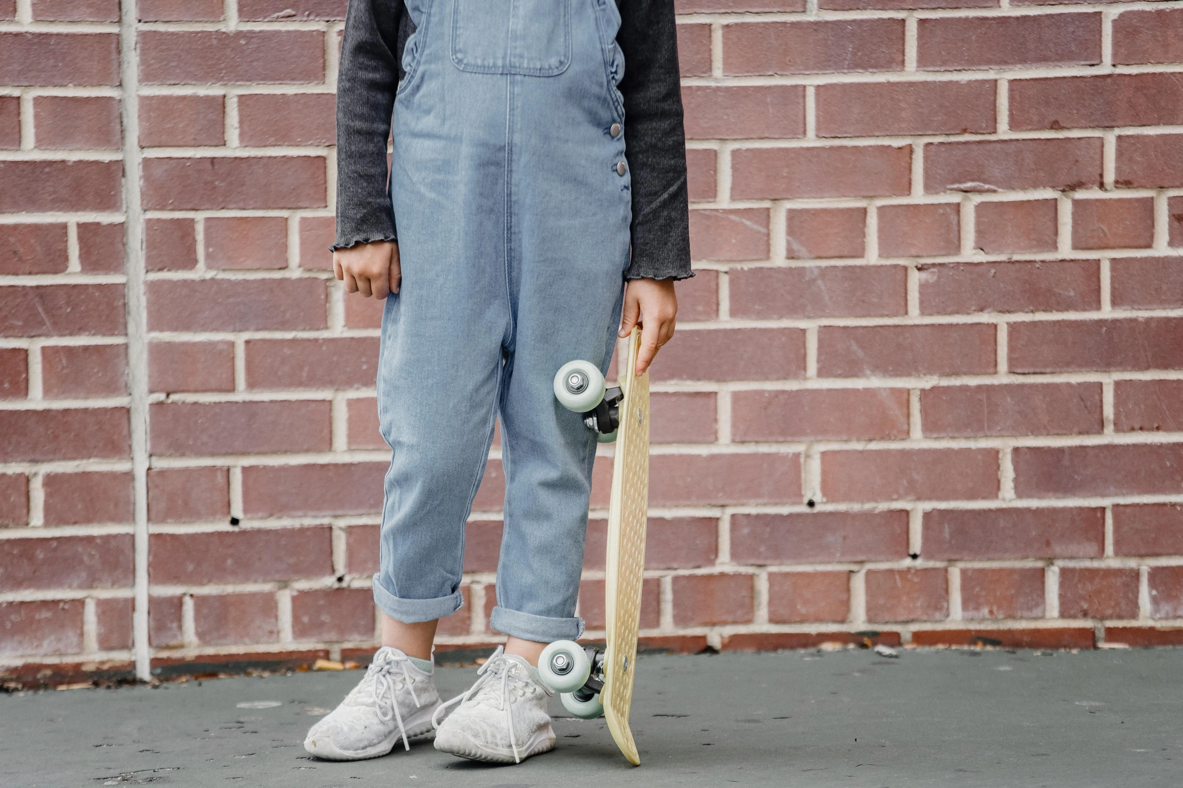 a person standing with a skateboard in front of a brick wall, by Helen Stevenson, trending on pexels, blue overalls, for kids, light grey, on grey background