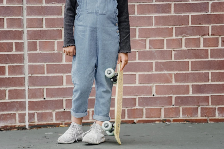 a person standing with a skateboard in front of a brick wall, by Helen Stevenson, trending on pexels, blue overalls, for kids, light grey, on grey background