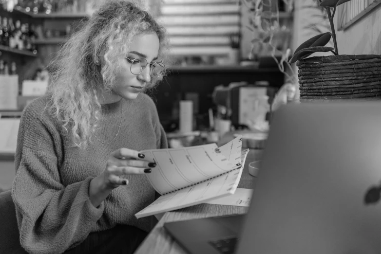 a black and white photo of a woman sitting in front of a laptop, a black and white photo, by Emma Andijewska, pexels, academic art, curly blonde hair | d & d, trying to read, at home, julia garner