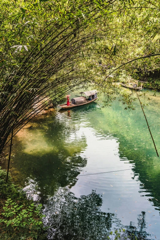 a boat floating on top of a river next to a lush green forest, bo xun ling, hot springs hidden cave, nezha, in a bamboo forest