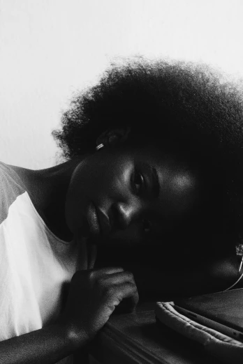 a woman sitting at a desk with her hand on her chin, a black and white photo, by Clifford Ross, pexels contest winner, light skinned african young girl, laying down, with afro, adut akech