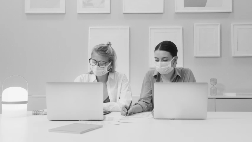 a couple of women sitting at a table with laptops, a black and white photo, by Emma Andijewska, pexels, computer art, masked doctors, dust mask, corporate animation style, busy room