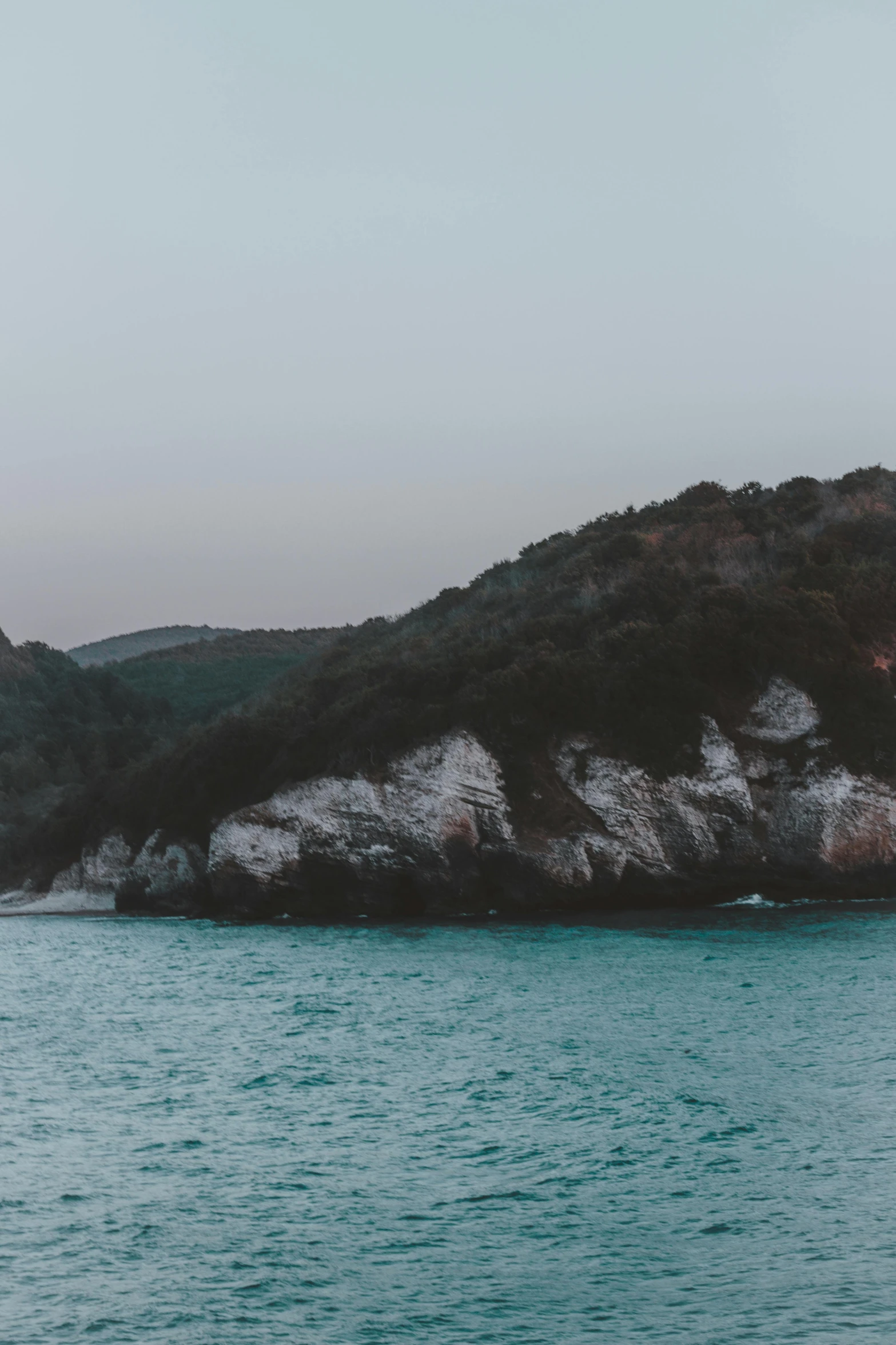 a body of water with a mountain in the background, inspired by Elsa Bleda, unsplash contest winner, romanticism, croatian coastline, cliff side at dusk, skull island, sunfaded