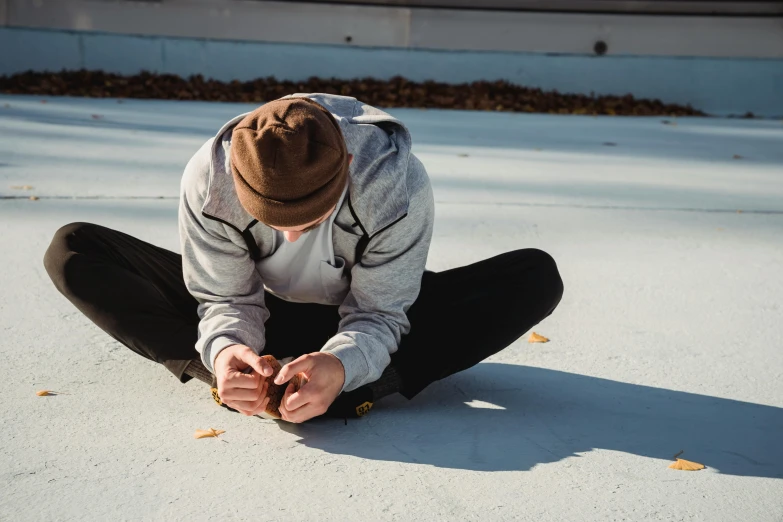 a man sitting on the ground looking at his cell phone, unsplash, visual art, he also wears a grey beanie, doing splits and stretching, looking down, 15081959 21121991 01012000 4k