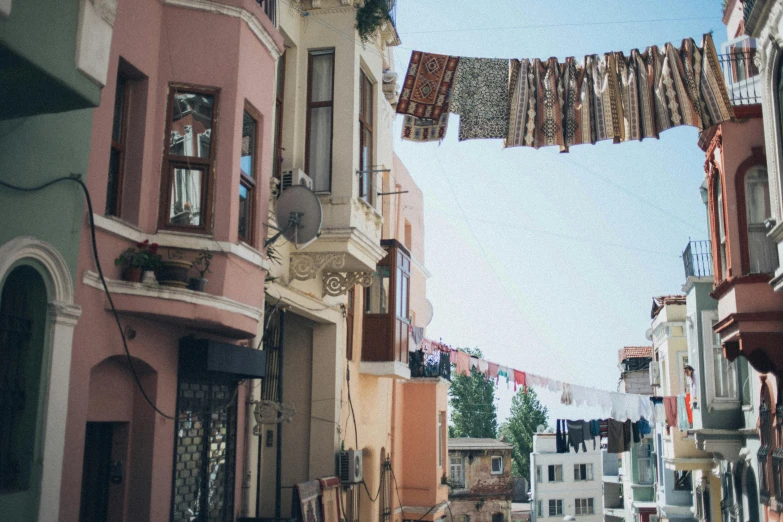 a group of people walking down a street next to tall buildings, a photo, inspired by Niyazi Selimoglu, pexels contest winner, renaissance, laundry hanging, mixture turkish and russian, pale colors, view from ground