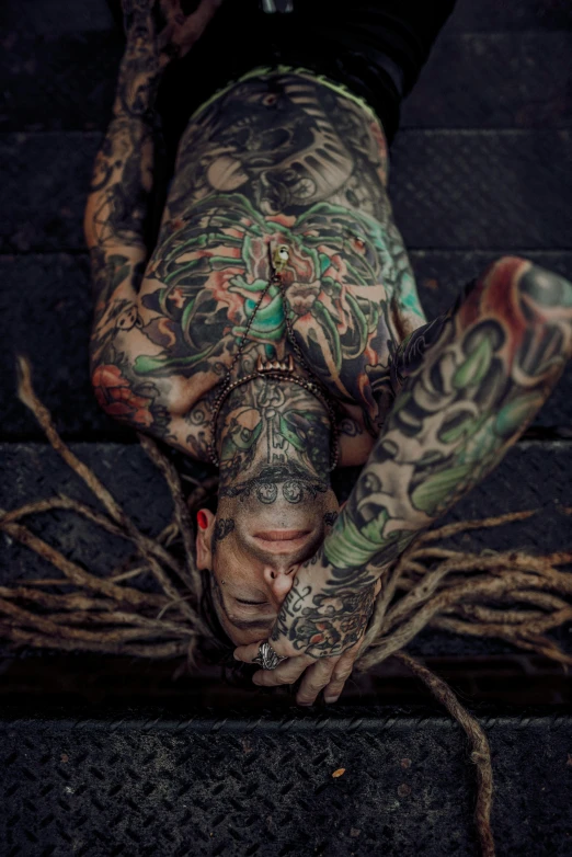 a man that is laying down on some stairs, a tattoo, pexels contest winner, hyperrealism, covered with roots, tattooed skin, 4 2 0, covered in vines