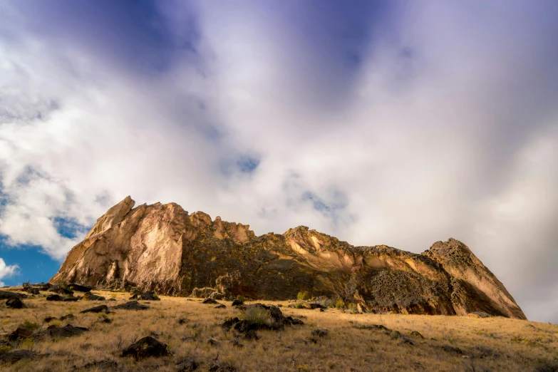 a mountain with a cloudy sky in the background, unsplash, les nabis, geological strata, mammoth, rocks flying, brown