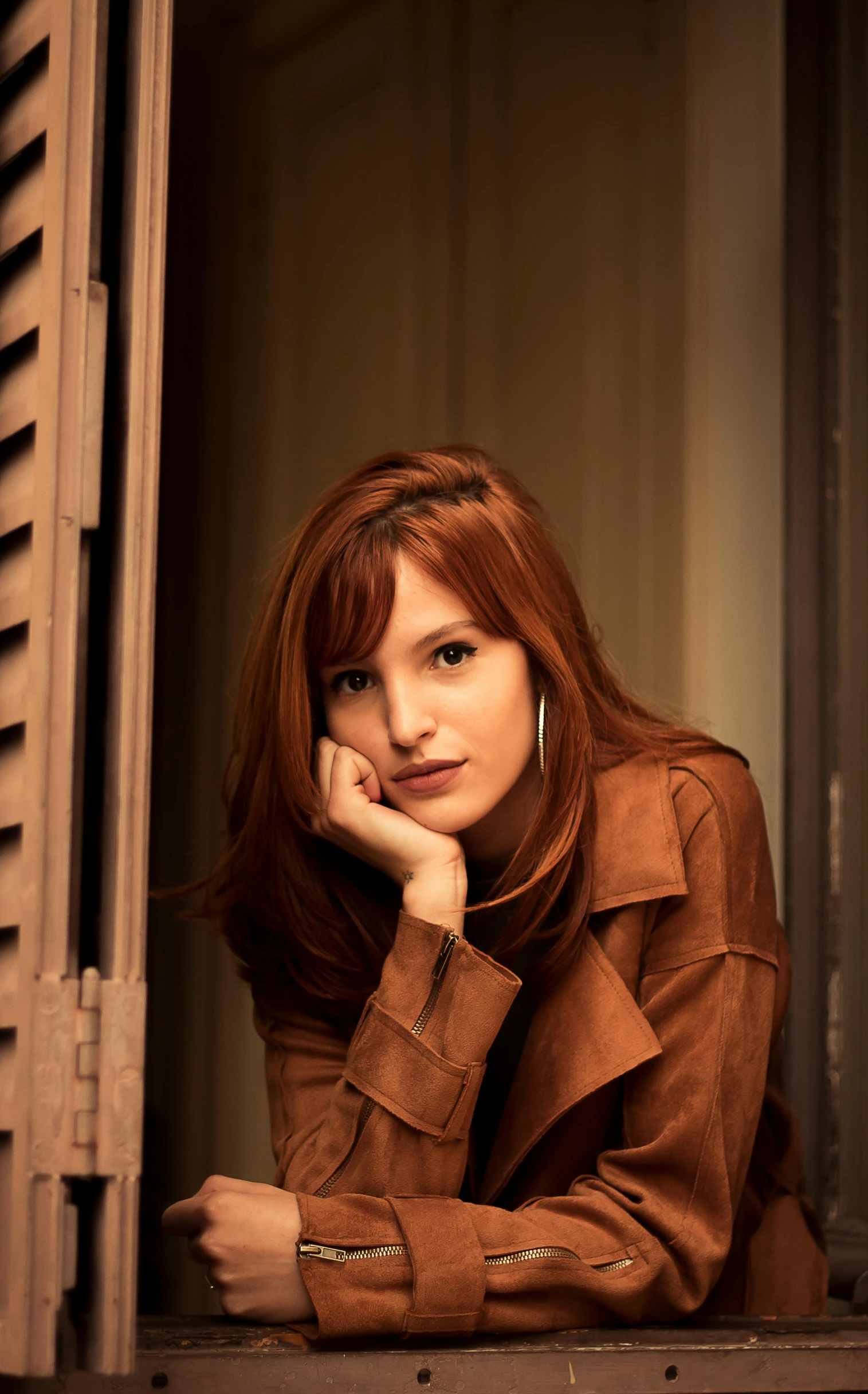 a woman leaning on a window sill with her hand on her chin, a portrait, flickr, brown red long hair, wearing brown leather jacket, promotional image, raphael personnaz