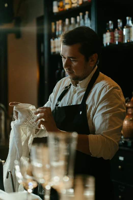 a man that is standing in front of a bar, pouring techniques, white waist apron and undershirt, looking serious, dry ice