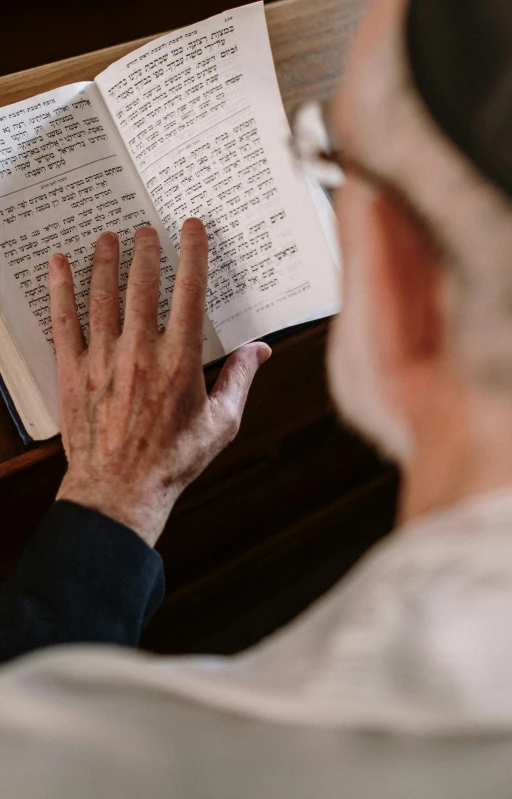 a man sitting at a table reading a book, by Leo Michelson, pexels, hebrew, pray, 15081959 21121991 01012000 4k, banner