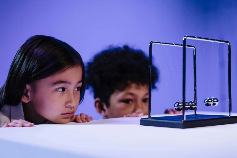 two children looking at an electronic device on a table, kinetic art, newton's cradle, projection mapping, toy guillotine, 8k award-winning photograph