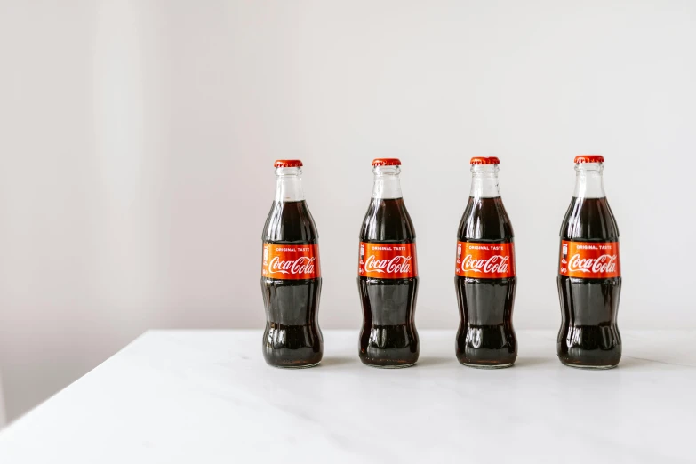 three bottles of coca cola sitting on a table, inspired by Dorothy Coke, unsplash, lined up horizontally, 6 pack, looking from side, traditional medium