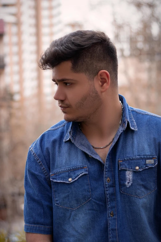 a young man standing in front of a tall building, an album cover, pexels contest winner, realism, mexican vaquero, headshot profile picture, wearing denim, lgbtq