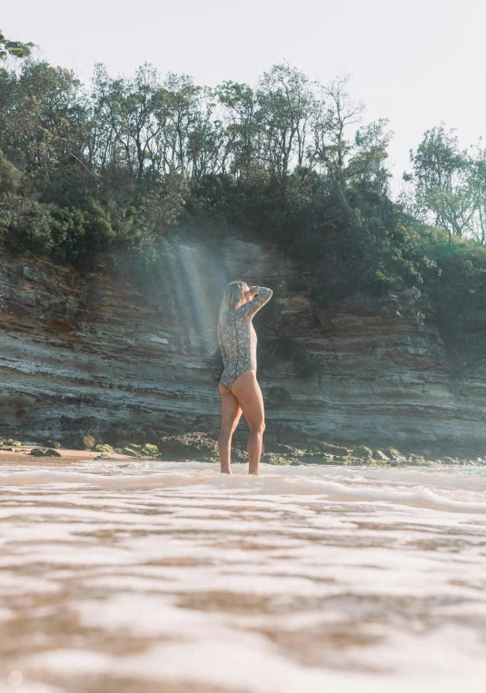 a person standing in the water with a frisbee, sandstone, on the beach at noonday, rays, liam brazier