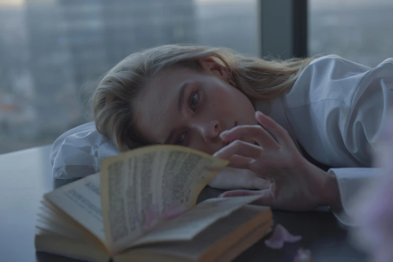a woman laying on top of a table next to a book, inspired by Elsa Bleda, pexels contest winner, hyperrealism, elizabeth olsen, soft light.4k, portrait of kim petras, sydney sweeney