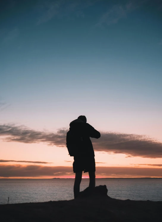 a man standing on top of a rock next to the ocean, a picture, pexels contest winner, romanticism, hugging, profile picture, a man wearing a backpack, ((sunset))