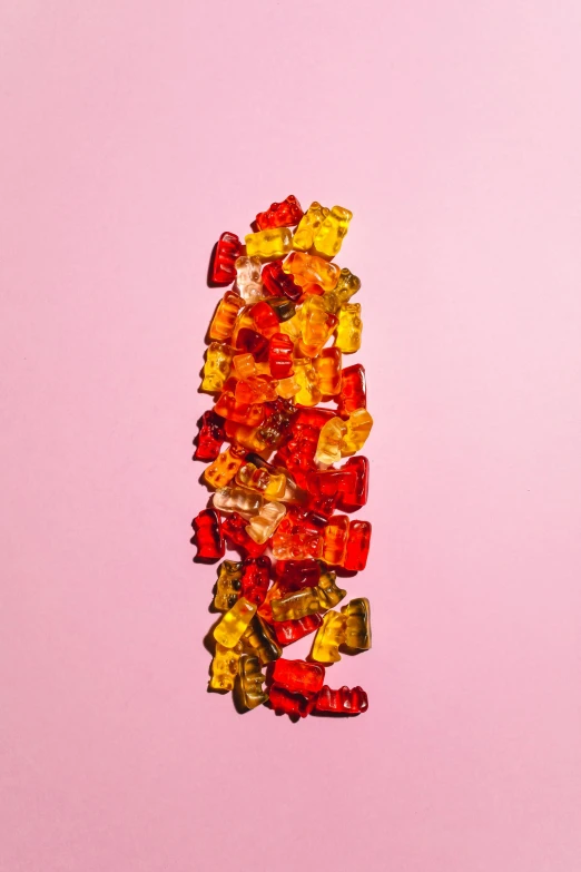 a pile of gummy bears sitting on top of a pink surface, by Jessie Algie, dark oranges reds and yellows, profile image, hegre, hemp