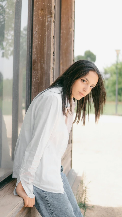 a woman leaning against a window in a white shirt, an album cover, inspired by Amelia Peláez, trending on unsplash, ana de la reguera portrait, wearing casual clothing, outside view, soft portrait shot 8 k