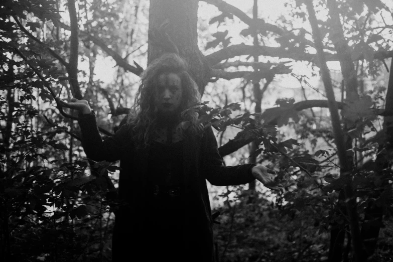 a black and white photo of a person in the woods, an album cover, inspired by Kati Horna, unsplash, conceptual art, black metal rococo, satanic ritual, slightly sunny, in a menacing pose