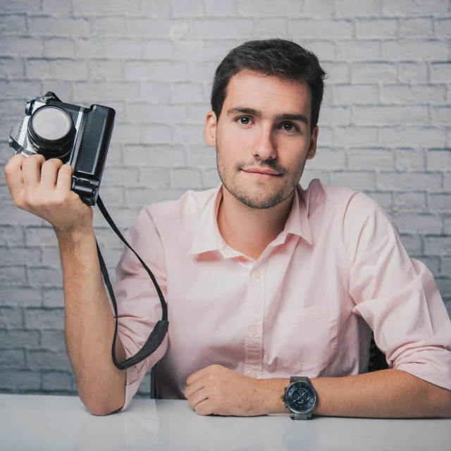 a man sitting at a table holding a camera, posing for a picture, adrian borda, avatar image, high quality photograph