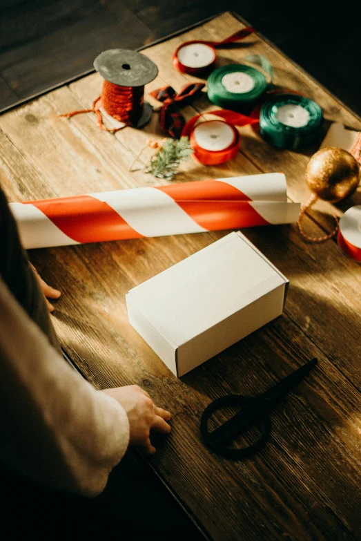 a person sitting at a table with a box and a pair of scissors, candy canes, designer product, thumbnail, wrapped