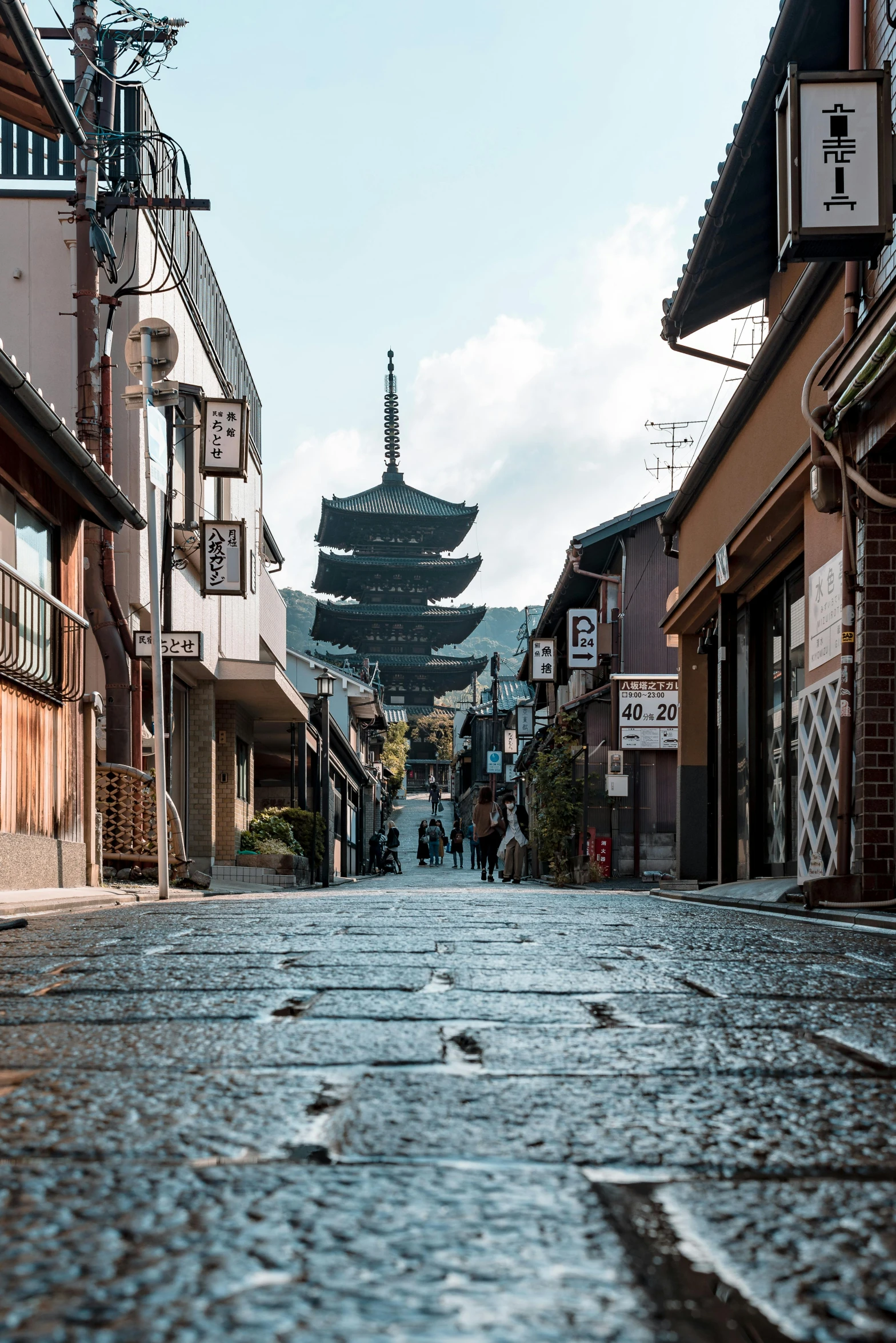 a cobblestone street with a pagoda in the background, inspired by Kanō Shōsenin, unsplash contest winner, mountains and a huge old city, lots of shops, extremely clear and coherent, very long spires