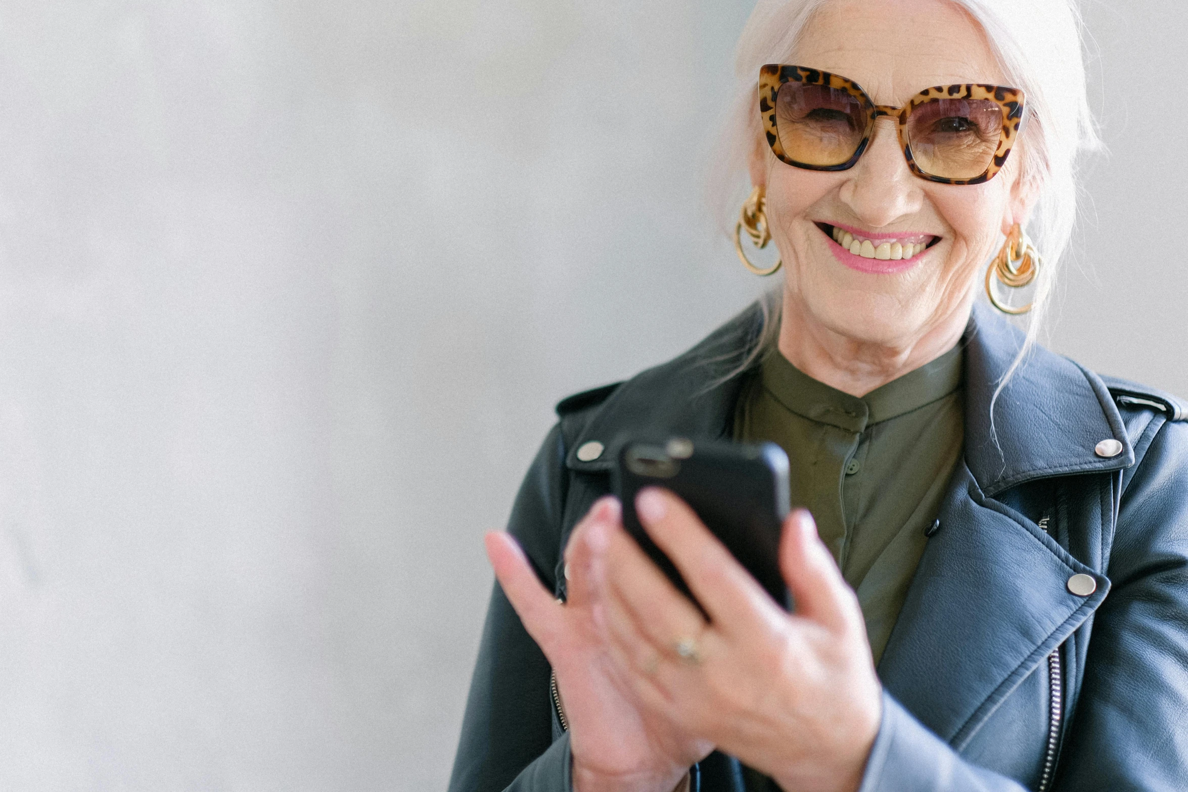 a close up of a person holding a cell phone, white haired lady, implanted sunglasses, standing elegantly, older woman