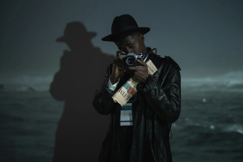 a man standing in front of a body of water holding a camera, an album cover, inspired by Gordon Parks, pexels contest winner, afrofuturism, noir detective and a fedora, under a spotlight, ( ( theatrical ) ), papa legba