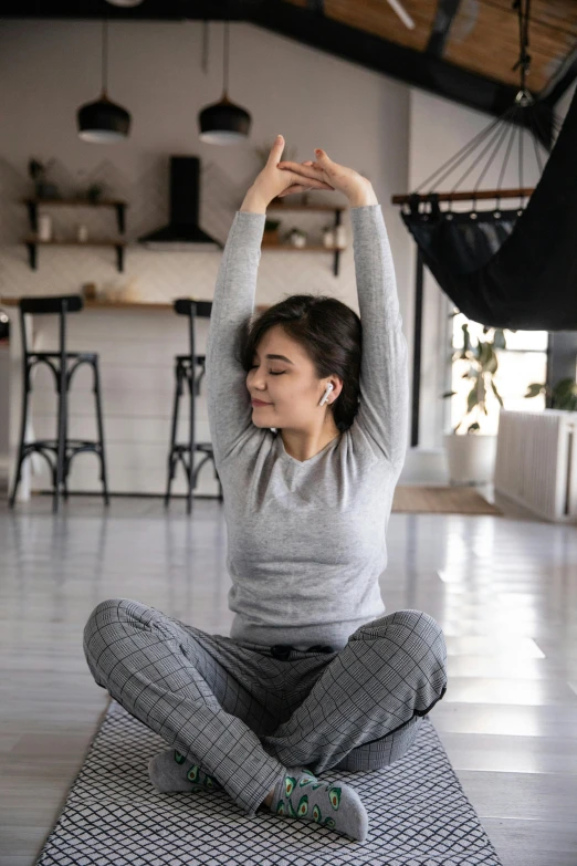 a woman sitting on a yoga mat doing a yoga pose, inspired by Li Di, trending on pexels, renaissance, wearing a track suit, grey, at home, square