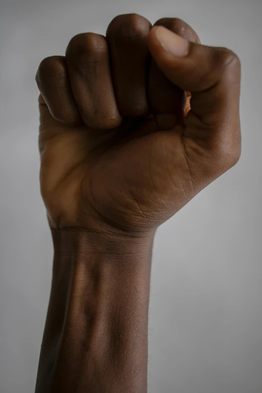 a close up of a person's fist, dark brown skin, on grey background, strong presense, left hand