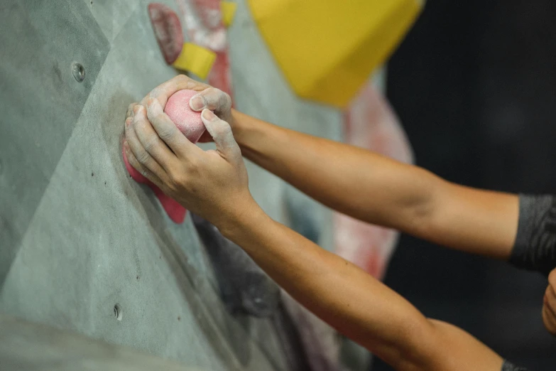 a close up of a person on a climbing wall, trending on pexels, partially cupping her hands, manuka, chalked, holding a ball