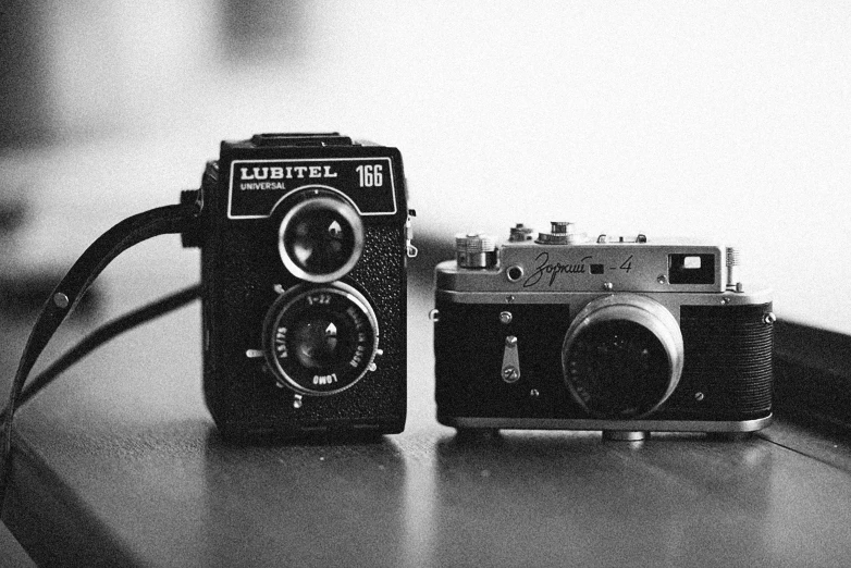 a couple of cameras sitting on top of a table, a black and white photo, by Andrée Ruellan, cinematic. by leng jun, retro dark vintage, daniel dociu, cute photo