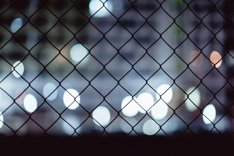 a view of a city through a chain link fence, inspired by Elsa Bleda, unsplash, window lights, dark. no text, unfocused, instagram post