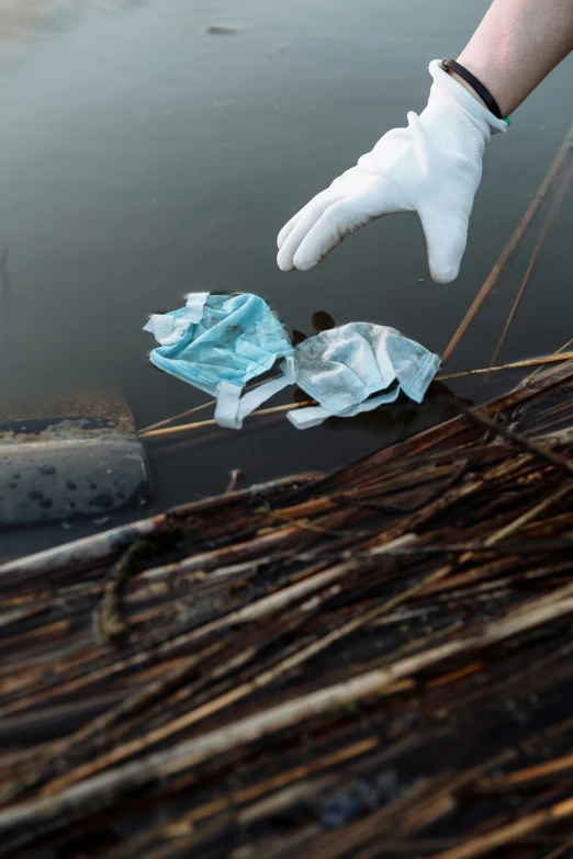 a person in white gloves next to a body of water, plasticien, recycled, promo image, concern, brown