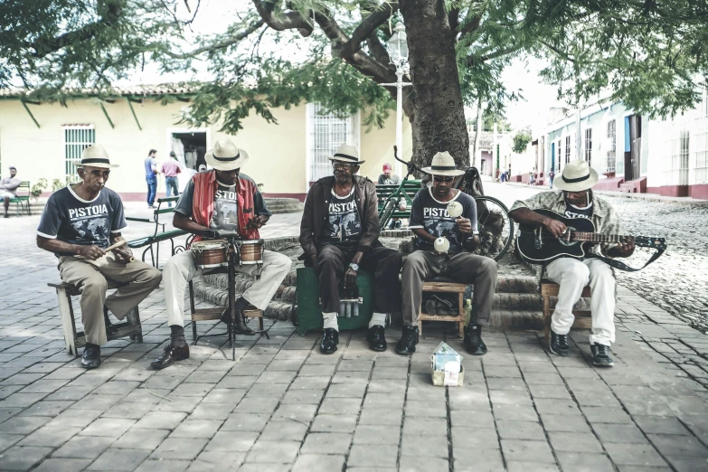 a group of men sitting next to each other on a bench, an album cover, by Ceferí Olivé, pexels contest winner, colonial era street, playing guitars, wearing a straw hat and overalls, touring