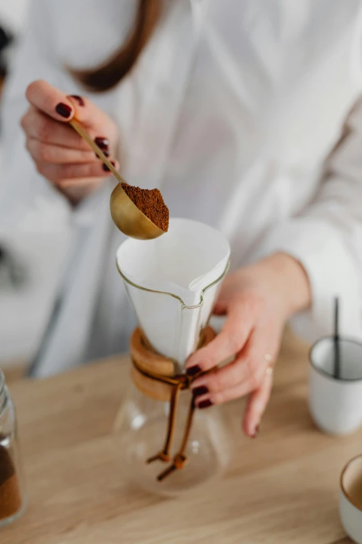 a woman is pouring a cup of coffee, by Julia Pishtar, spoon placed, cone shaped, beakers, zoomed in