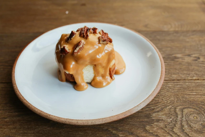 a white plate topped with a donut covered in caramel, inspired by Richmond Barthé, unsplash, bun, a wooden, cheesy, cut-away