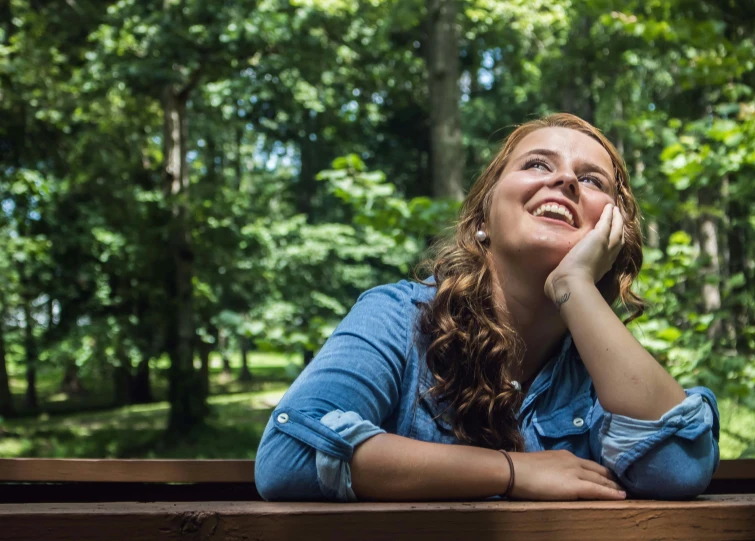 a beautiful young woman sitting on top of a wooden bench, a portrait, by Meredith Dillman, unsplash, happening, looking upward, lush surroundings, smiling slightly, college