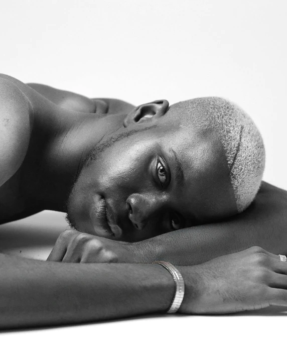 a black and white photo of a naked man, inspired by Theo Constanté, trending on unsplash, afrofuturism, relaxed dwarf with white hair, laying down with wrists together, non binary model, looking off to the side