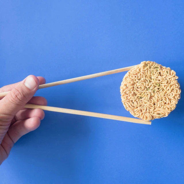 a person holding chopsticks over a bowl of noodles, with a blue background, miniature product photo, reverse, round-cropped