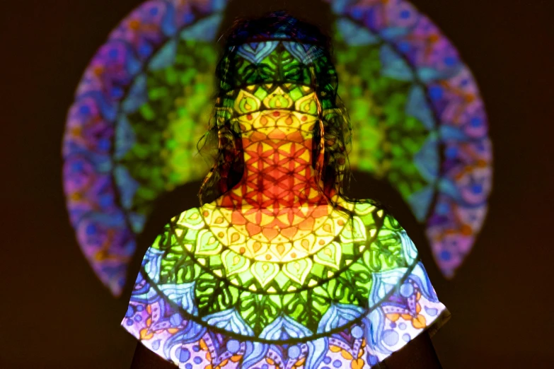 a woman that is standing in the dark, a hologram, inspired by Alex Grey, interactive art, intricate stained glass, rave otufit, sitting down, vibrant backlit