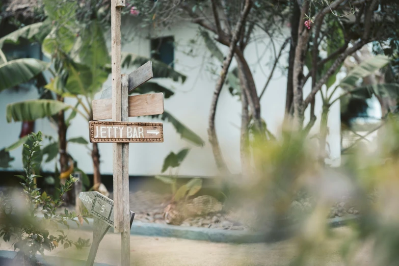 a wooden sign sitting on the side of a road, sol retreat, courtyard walkway, on the coast, blurry