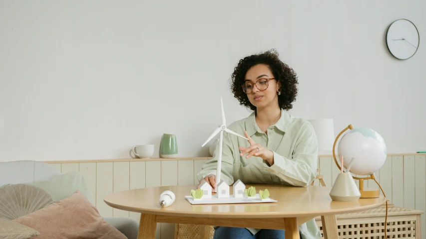 a woman sitting at a table with a model of a house, pexels contest winner, kinetic art, wind turbines, avatar image, people sitting at tables, product introduction photo