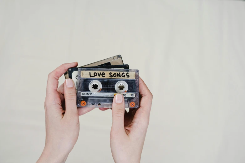 a person holding a cassette in their hands, an album cover, trending on pexels, love os begin of all, toys, a 35mm photo, on a pale background