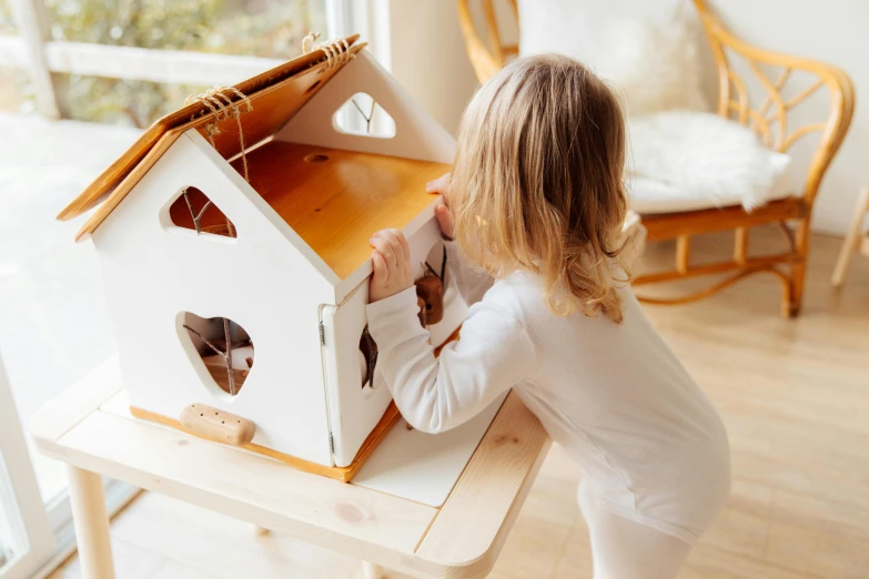 a little girl is playing with a doll house, by Julia Pishtar, white with chocolate brown spots, activity play centre, holding a wood piece, close face view