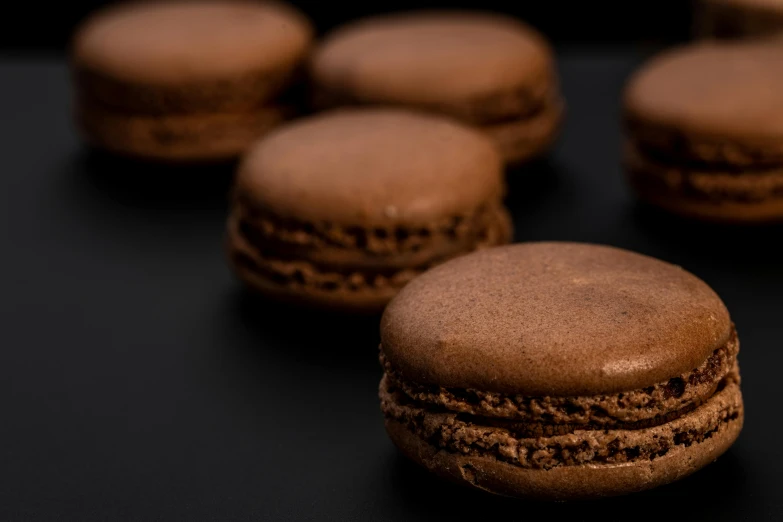 a group of chocolate macarons sitting on top of a table, a macro photograph, trending on pexels, with a black background, 15081959 21121991 01012000 4k, round-cropped, thumbnail