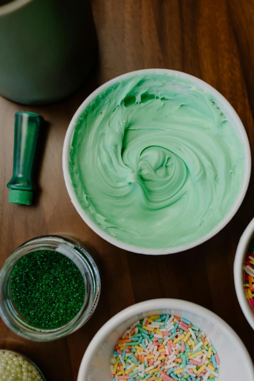 a wooden table topped with bowls of frosting and sprinkles, inspired by Art Green, trending on pexels, process art, green slime, products shot, greens, medium close shot