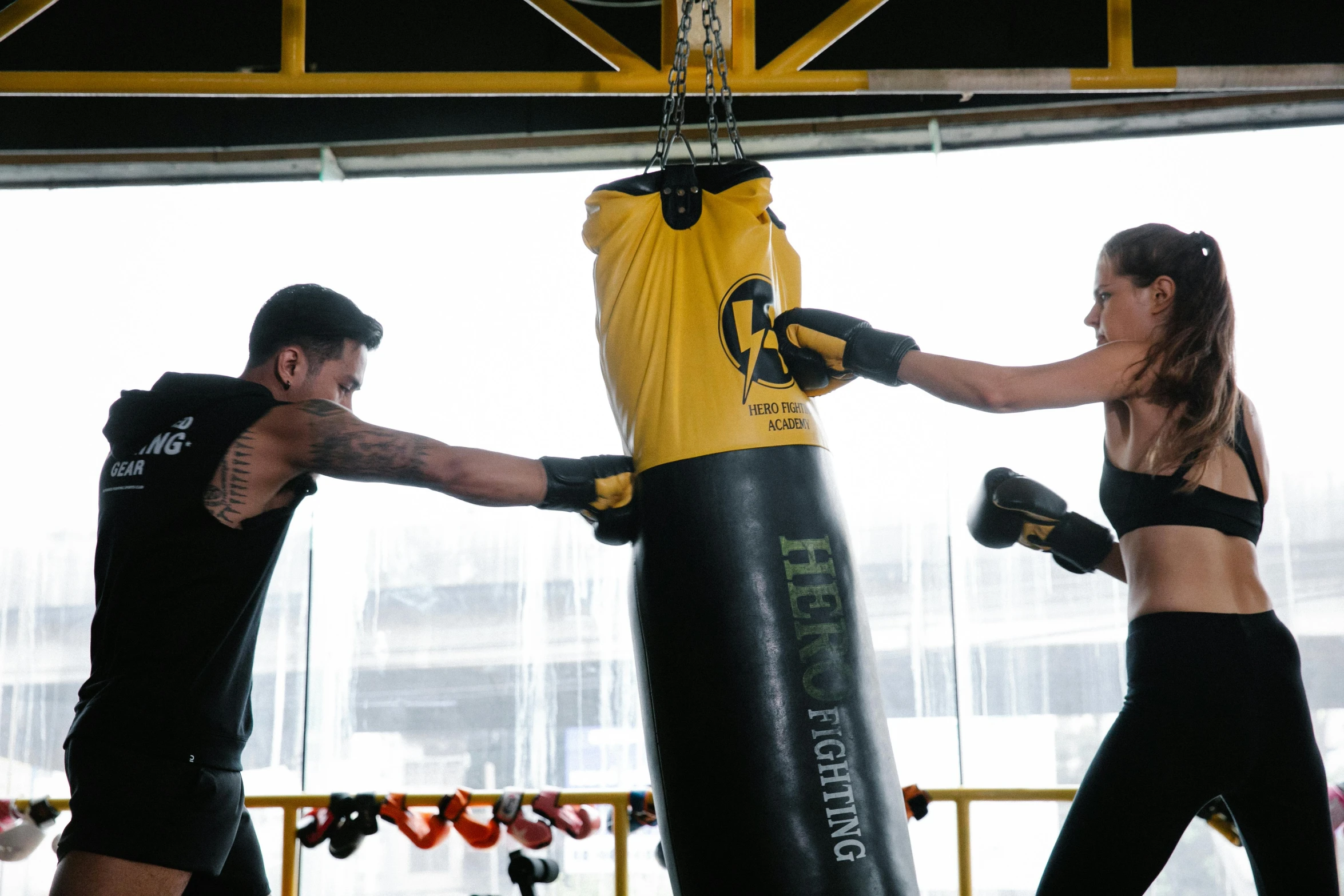 a man and a woman boxing in a gym, by Robbie Trevino, hurufiyya, yellow and black, punching in a bag, profile image, central hub