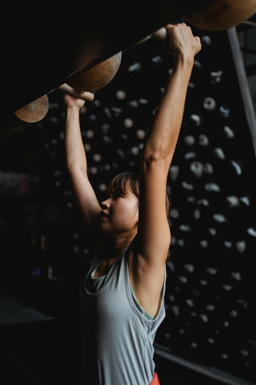 a woman holding a skateboard above her head, by Jessie Algie, pexels contest winner, happening, lifting weights, rock wall, scientific photo, dim dingy gym