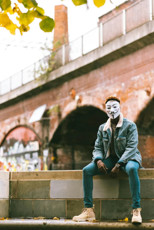 a man wearing a mask sitting on a wall, pexels contest winner, non binary model, 2019 trending photo, revolutionary, uk